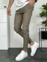 Muške braon pantalone regural fit kroja. Slika modela sa prekrštenim nogama i kombinacije sa belim patikama.