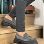 Muške kožne cipele sa visokim đonom u tamnosivoj boji. Prevrnuta koža. Slika modela u kombinaciji sa sivim pantalonama. Slika u stojećem položaju.