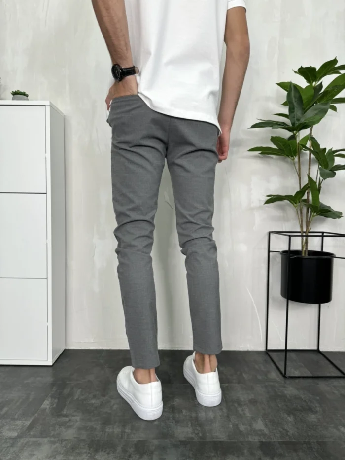 Muške sive pantalone slim fit kroja, prikazane sa zadnje strane, model nosi bele patike i belu majicu.