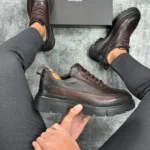 Muške zimske cipele od prave kože u braon boji, model drži cipele u ruci.