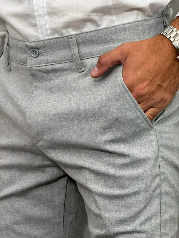 Detaljan prikaz džepa i pojasa na prednjoj strani muških sivih pantalona.