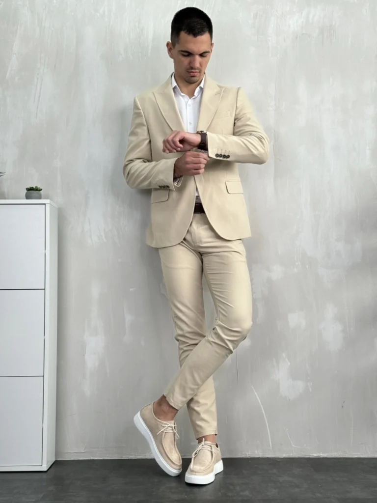 Muško odelo u bež boji, slim fit kroj, model stoji i gleda na sat.